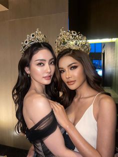 two beautiful young women standing next to each other in front of a mirror wearing crowns