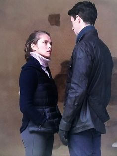 a man and woman standing next to each other in front of a wall with peeling paint on it