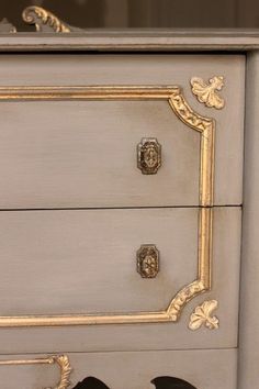 an antique dresser with gold trimmings and black birds on the drawer knobs