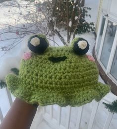 a crocheted frog hat is held up in the snow