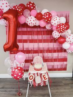 a red and white birthday party with balloons, streamers and cake on a chair