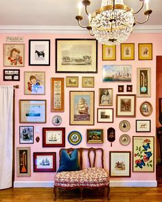 a pink wall with many framed pictures and a chandelier hanging from the ceiling