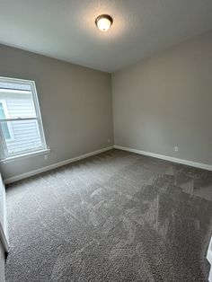 an empty room with carpeted floors and a window in the corner on the far wall