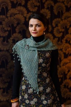 a woman standing in front of a wall wearing a green scarf and black dress with flowers on it