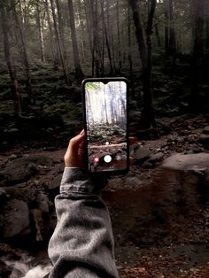 someone is holding up their cell phone to take a photo in the woods with trees