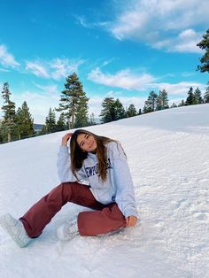 a woman sitting in the snow with her feet up and arms behind her head, smiling at the camera