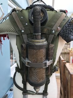 a mannequin dressed in an army green vest and gas mask with metal parts attached to it