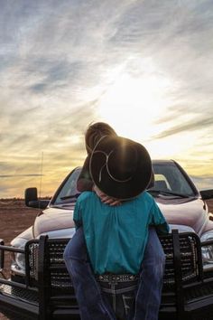 a man sitting on the back of a truck in front of a white pickup truck