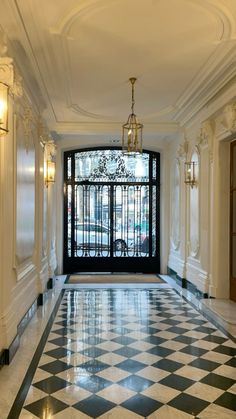 a hallway with black and white checkered flooring, chandelier and windows