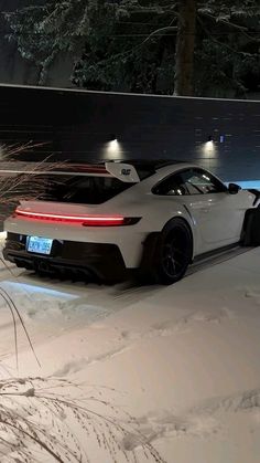 a white sports car driving down a snow covered road at night with its lights on