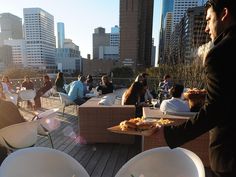 people are sitting at tables on a roof deck with white chairs and plates in front of them