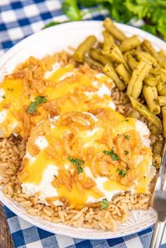 a white plate topped with rice covered in cheese next to green beans and asparagus