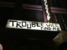 a sign that reads trouble will find me on the side of a building at night