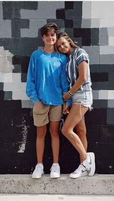 two people standing next to each other in front of a wall