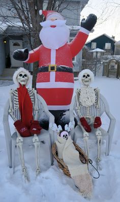 three skeletons sitting on chairs in the snow next to a santa clause balloon and skeleton decorations