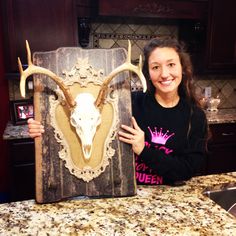 a woman is holding up an animal skull in front of a wooden plaque that has been carved into it