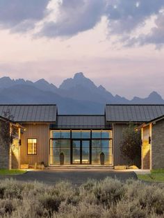 a house that is sitting in the grass with mountains in the backgroup