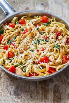 a skillet filled with pasta, chicken and tomatoes on top of a wooden table