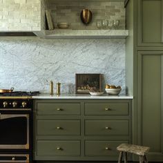 a kitchen with green cabinets and marble counter tops, gold trimming on the stove