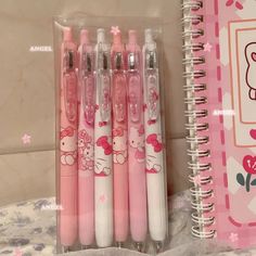 four pink hello kitty pens sitting next to each other on a table with a notebook