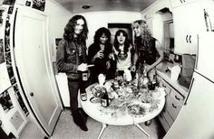 four women standing around a kitchen table with food on it and drinks in front of them