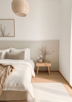 a bedroom with white walls and wood flooring is pictured in this image, there are two lamps hanging above the bed