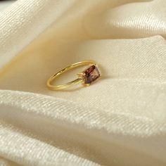 a gold ring with a brown stone on it sitting on a white cloth covered surface