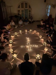 a group of people sitting in a circle with lit candles on the floor around them