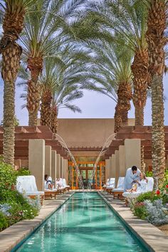 two people sitting on lounge chairs next to a large pool with water running through it