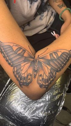 a butterfly tattoo is on the arm of a person sitting in a chair with their hands together