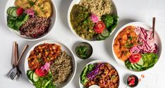 several bowls of food are arranged on a white table top, including salads and pita chips