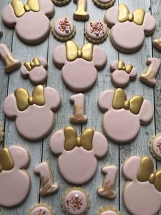 pink and gold mickey mouse cookies are arranged on a wooden table with other decorated cookies