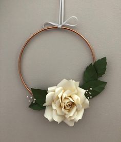 a white rose is hanging on the wall next to a metal hoop with leaves and pearls