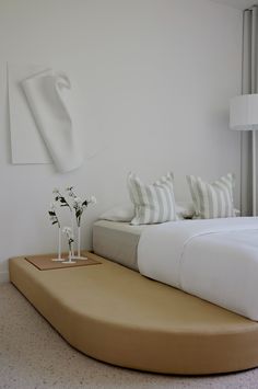 a bed with white sheets and pillows on top of it next to a vase filled with flowers