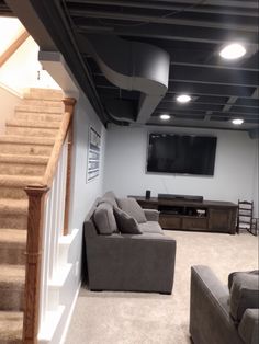 a living room filled with furniture and a flat screen tv mounted to the wall next to a stair case