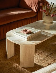 a coffee table with a book on it in front of a couch and flower vase