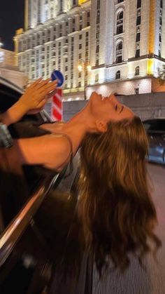 a woman sticking her head out the window of a car in front of a building