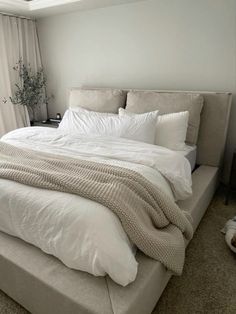 a bed with white sheets and pillows in a bedroom next to a window, near a plant