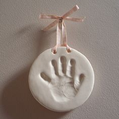 a white ceramic ornament with a hand print on it hanging from a pink ribbon