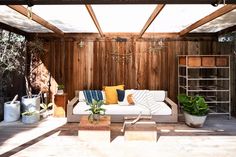 an outdoor living room with wood paneling and white couches, potted plants and hanging lights