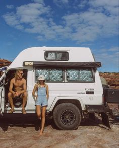 a man and woman sitting in the back of a white van on top of a dirt field