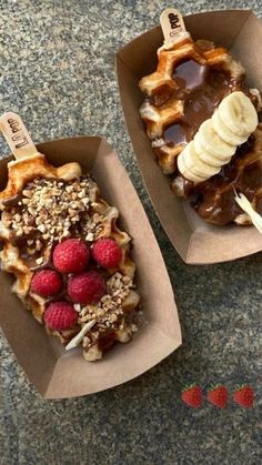 two waffles with bananas, raspberries and chocolate on top are sitting in cardboard boxes