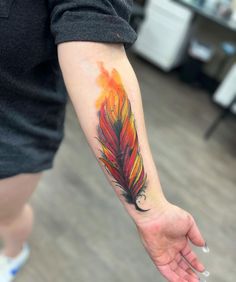 a person with a tattoo on their arm that has a red and yellow feather on it