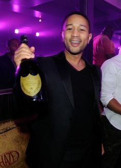 a man in a tuxedo holding up a bottle of wine at a party