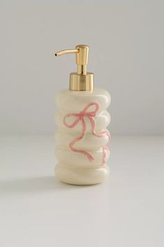 a white soap dispenser with pink ribbon on the front and gold faucet