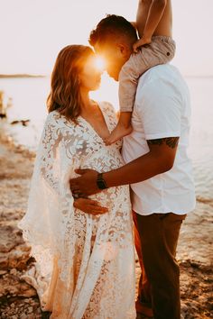 a man and woman standing next to each other on the beach with sun behind them