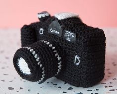 a crocheted camera sitting on top of a table next to a pink wall