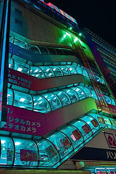 a tall building with neon lights on it's sides and windows at night time