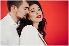 a man and woman with red lipstick on their lips are looking at each other while standing in front of a red background