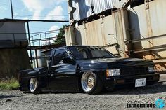 a black car is parked in front of a train track and some rusted metal structures